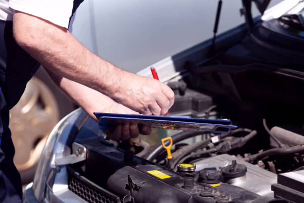 Auto mechanic checking car engine and writing on the clipboard